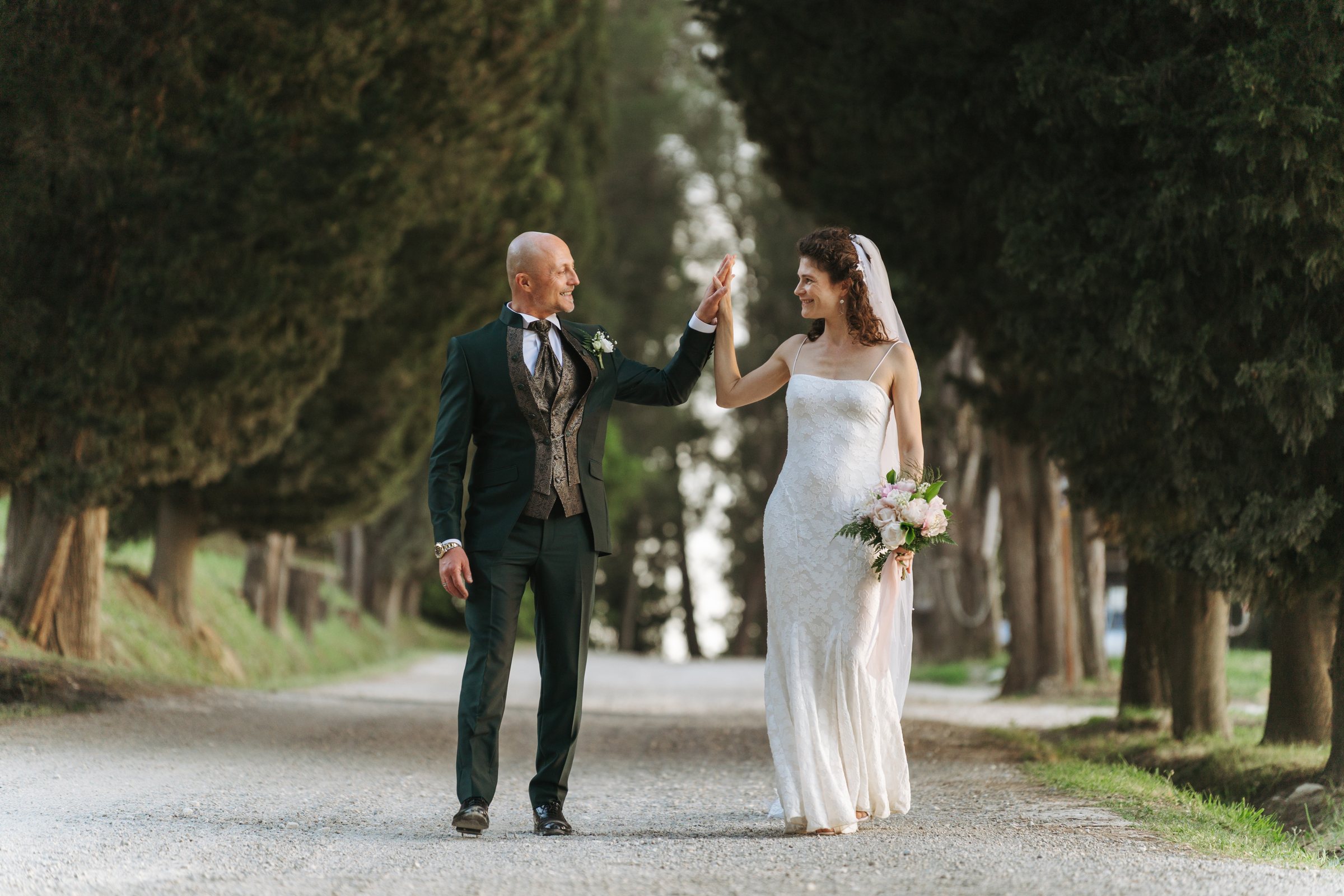 Alessio ed Erika si scambiano un gesto complice sul viale alberato