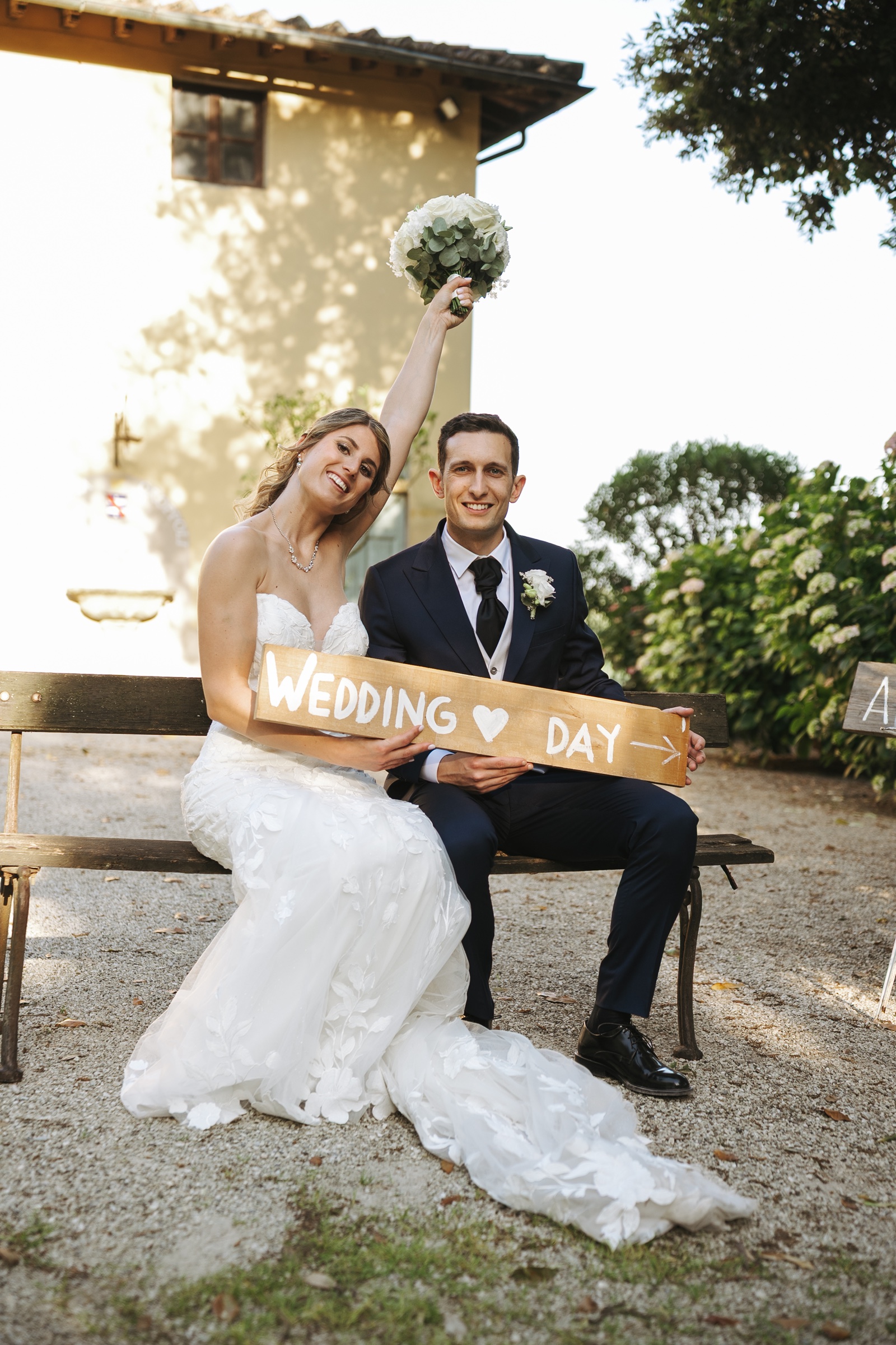 Simone e Giulia sorridono con il cartello del loro wedding day